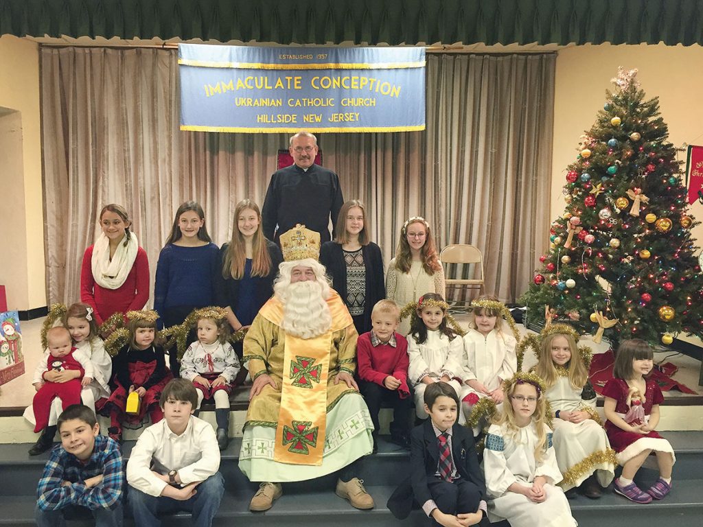 HILLSIDE, N.J. – St. Nicholas visited the children and parishioners of Immaculate Conception Ukrainian Catholic Church here on Sunday, December 6, 2015. He said he was inspired by the children’s love of their faith and their passionate request to have their religious education classes despite a very busy Sunday and traditional day off. Children age 3-18 years old participate in the parish’s religious education program. The children honored St. Nicholas by presenting a bilingual holiday entertainment program that consisted of a play and performances of Christmas music by young musicians and singers. Above, St. Nicholas is seen with the children and the parish administrator, the Rev. Vasyl Vladyka. – Joe Shatynski